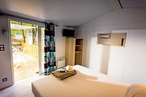Ein Schlafzimmer mit Bett, einem Fenster mit Vorhängen, einem an der Wand montierten Fernseher und einem kleinen Regal.