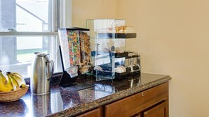 A kitchen counter with a coffee pot, a fruit basket, and a breakfast bar with cereal and bread. - Econo Lodge Sharon - Foxborough (Sharon)