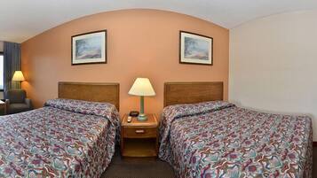 A hotel room with two beds, a nightstand with a lamp, a chair, and two framed pictures on the wall.