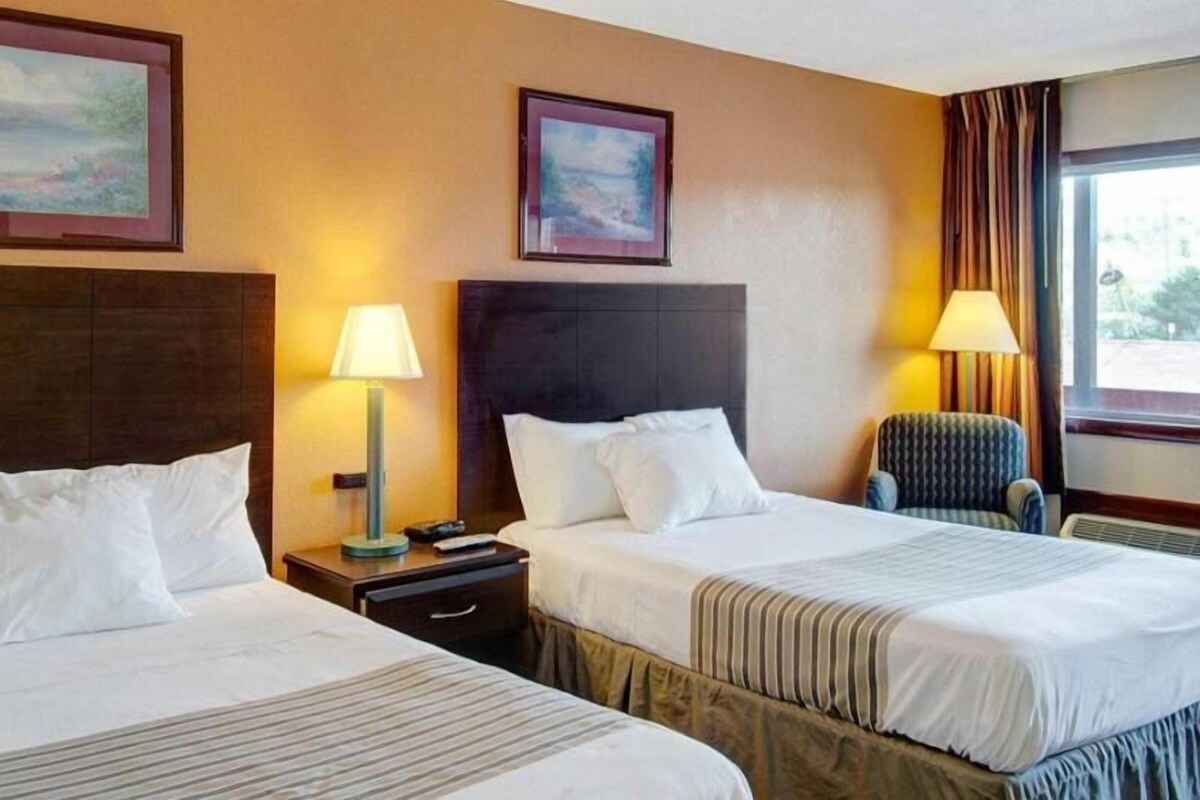 Habitación de hotel con dos camas, una mesita de noche, una lámpara, una silla y una ventana.