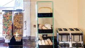 A breakfast bar with cereal, bread, pastries, and a toaster. - Econo Lodge Sharon - Foxborough (Sharon)