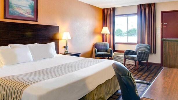 A hotel room with a large bed, two armchairs, a desk, and a window with curtains. - Econo Lodge Sharon - Foxborough (Sharon)