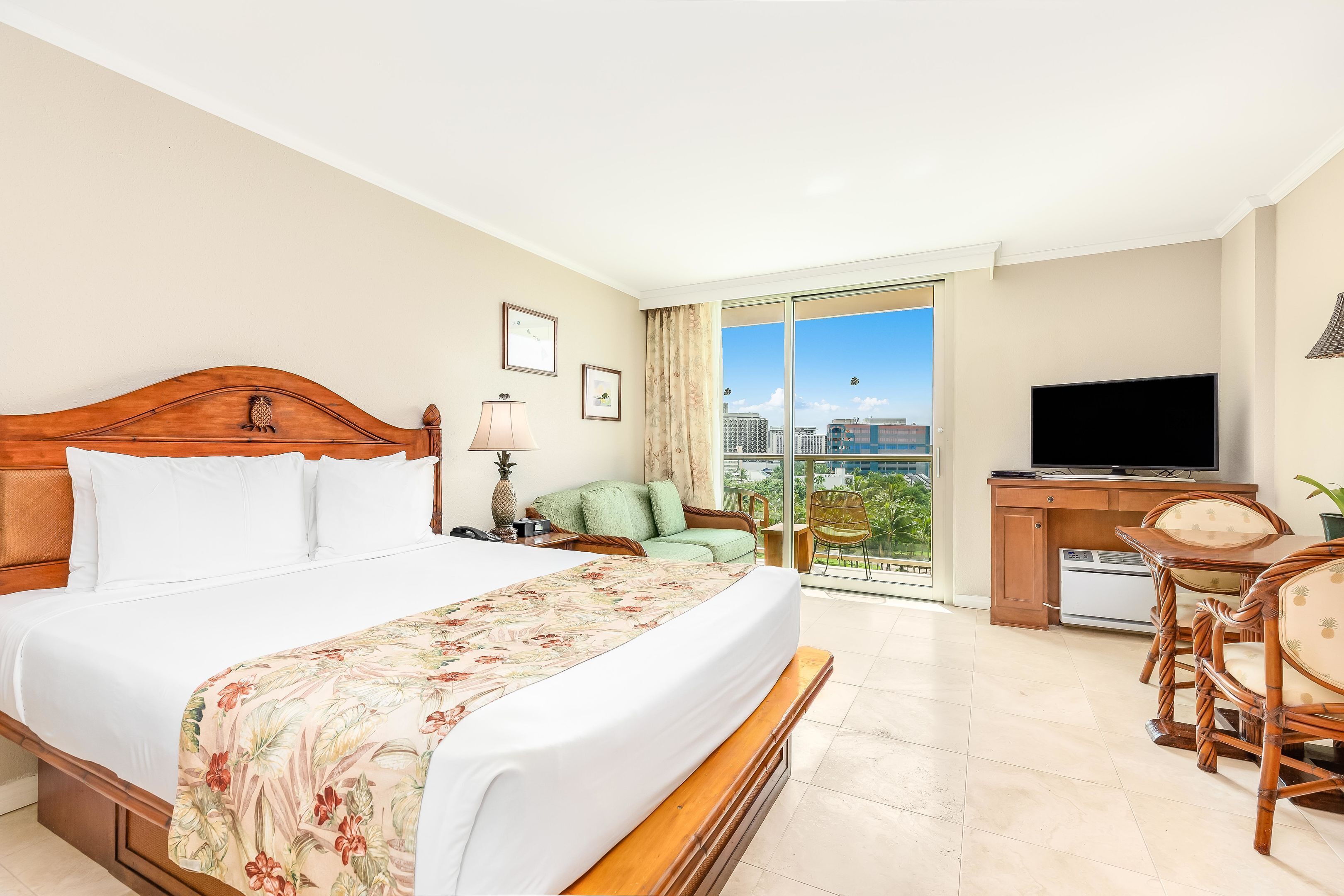 A hotel room with a bed, a desk with a television, a chair, and a view of the city.