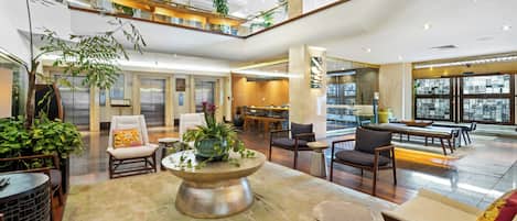 A spacious lobby with multiple seating areas, a central decorative table, and a high ceiling with natural light.