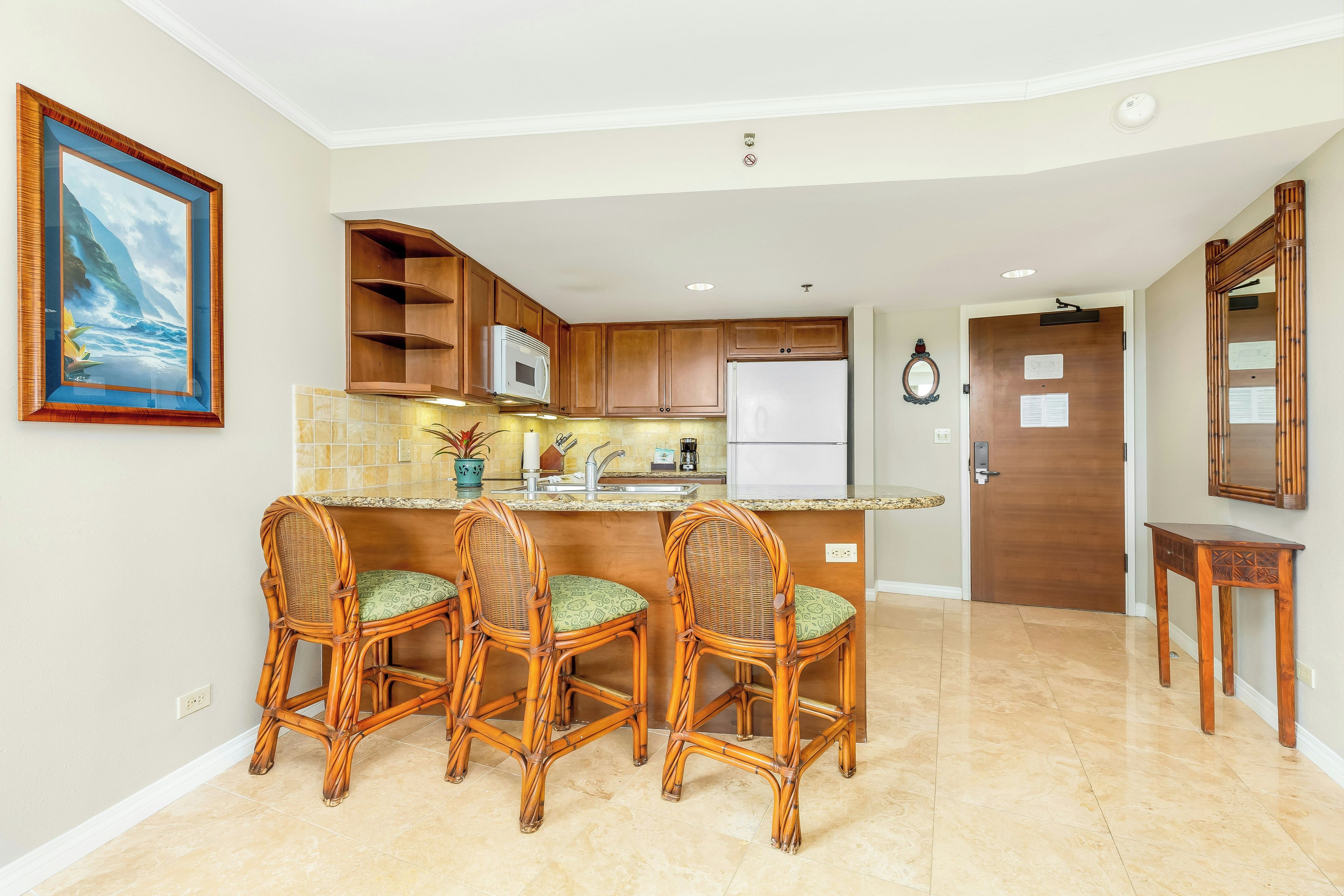 A kitchen with a central island, bar stools, wooden cabinets, a microwave, and a refrigerator.