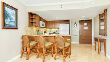 A kitchen with a central island, bar stools, wooden cabinets, a microwave, and a refrigerator.