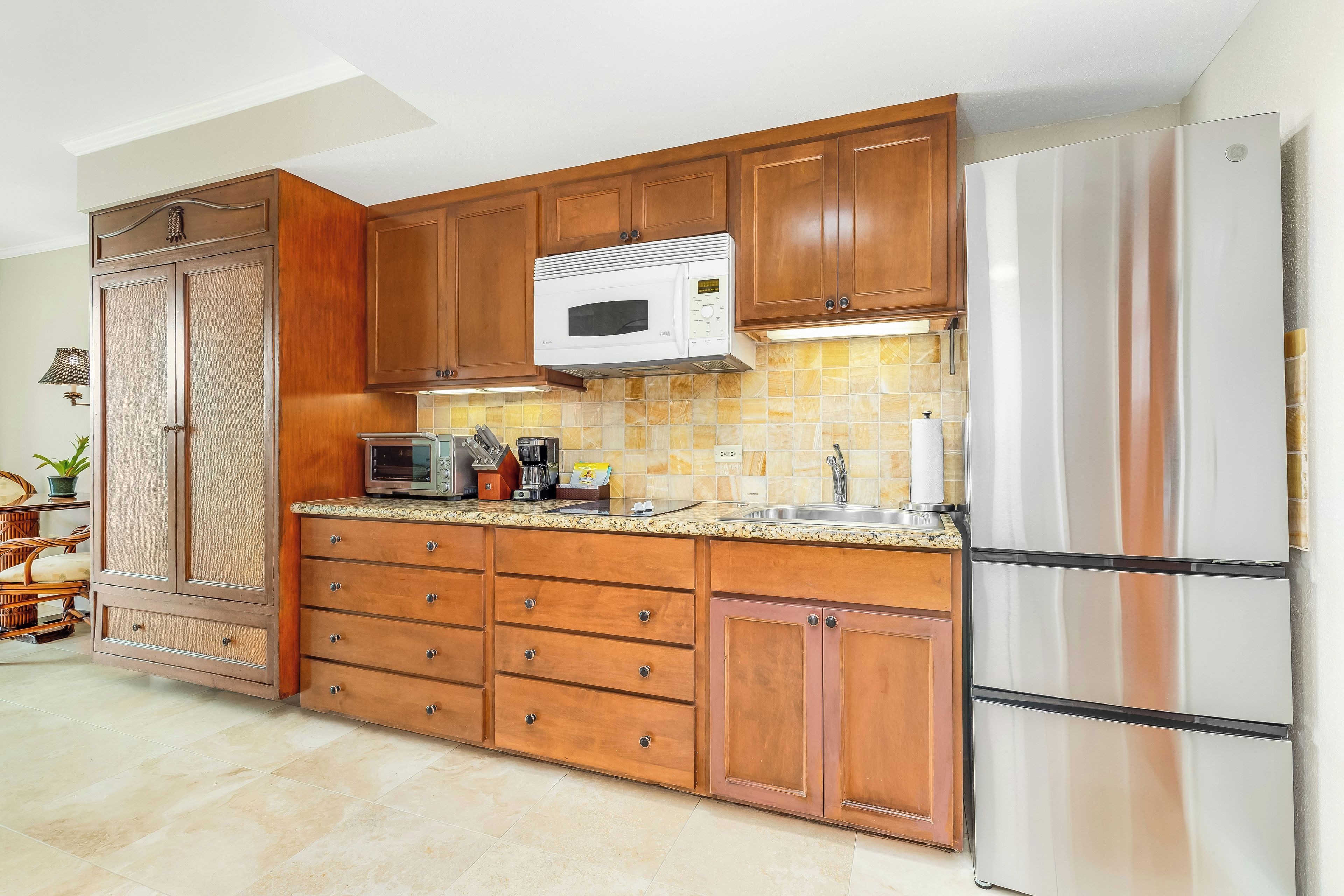 A kitchen with wooden cabinets, a microwave, a refrigerator, and a tiled backsplash.