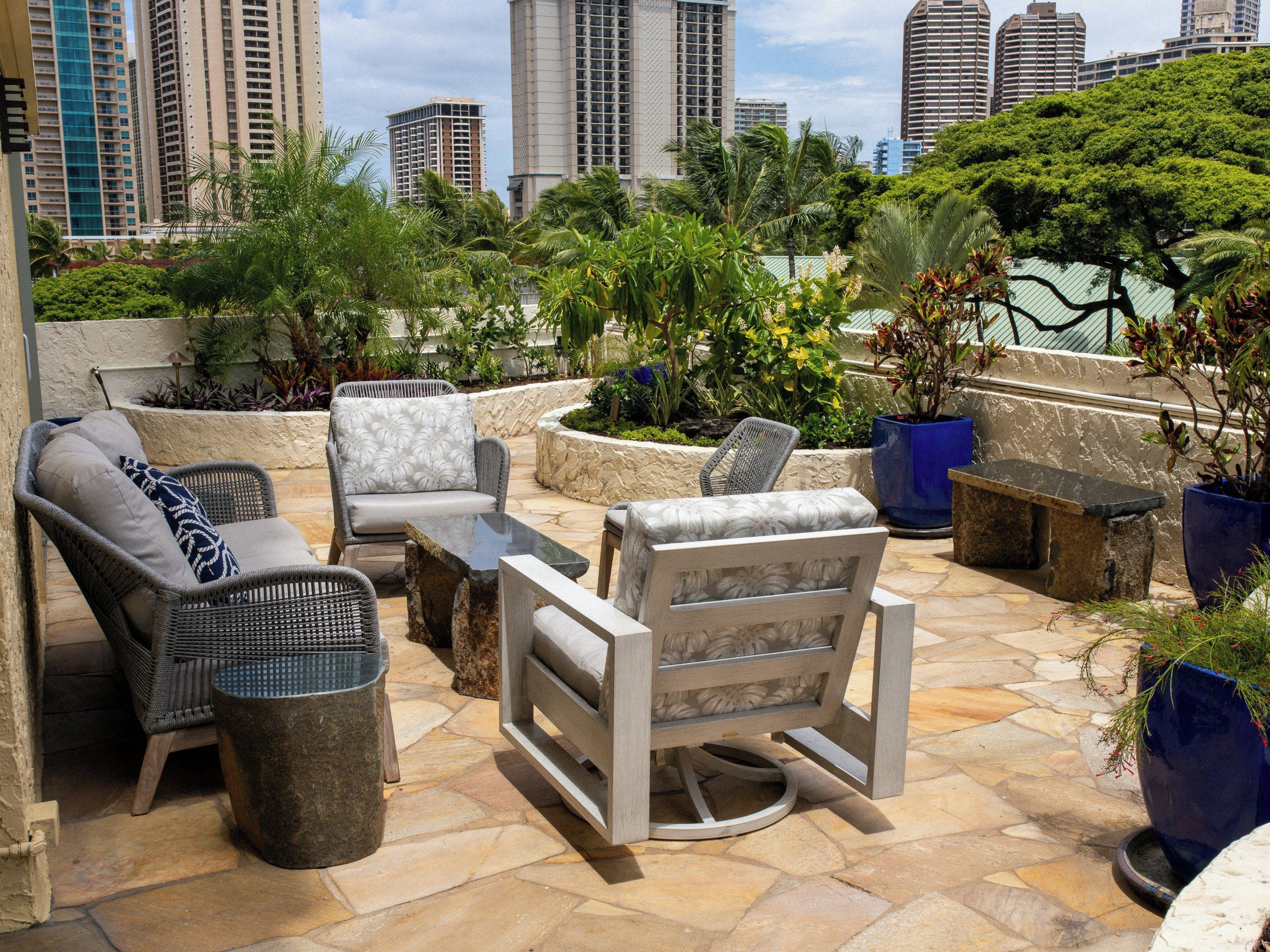 An outdoor seating area with wicker furniture and planters, overlooking a cityscape.