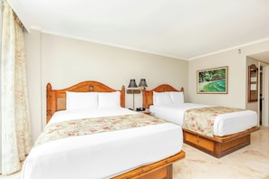 A hotel room with two wooden beds, white bedding, a painting on the wall, and a door leading to another room. - Luana Waikiki Hotel & Suites (Honolulu)