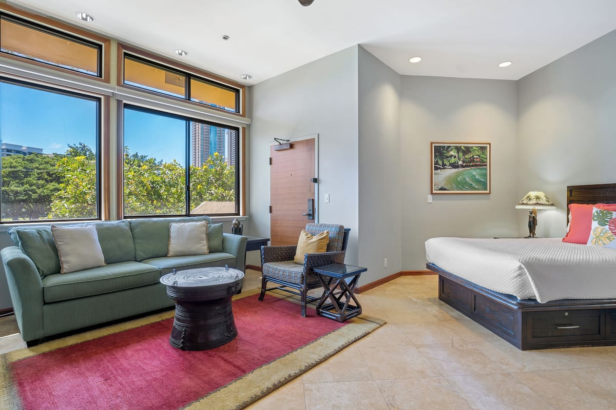 A modern bedroom with a large window, a sofa, a chair, a small table, and a bed.