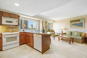 A kitchen with a built-in microwave, stove, and dishwasher. There is a dining area with a table and chairs. - Luana Waikiki Hotel & Suites (Honolulu)