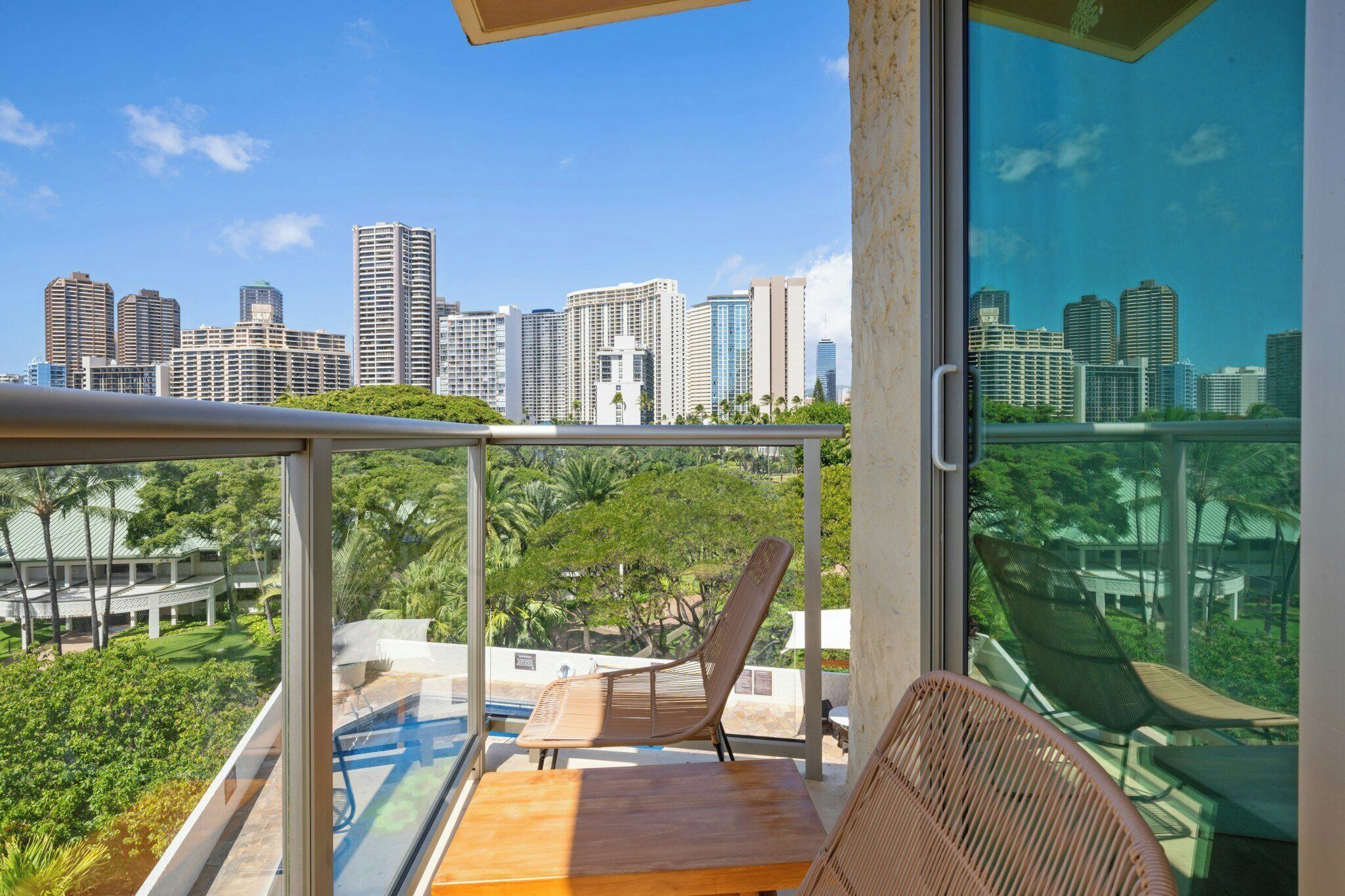 A balcony with a view of a city skyline, a wooden table, and a wicker chair.