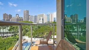 Un balcon offrant une vue sur les toits d’une ville, une table en bois et une chaise en osier.