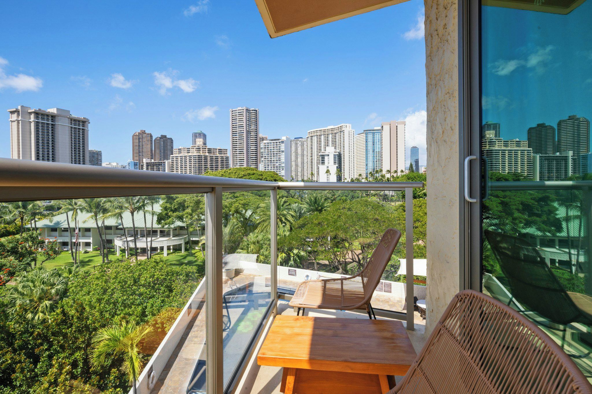 A balcony with a wooden table and chairs, overlooking a cityscape and lush greenery.