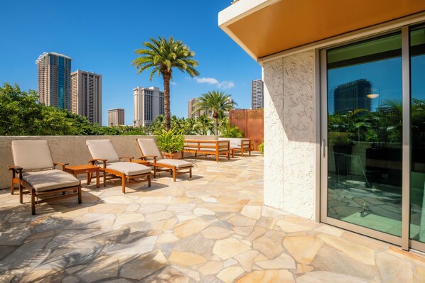 A rooftop patio with stone flooring, outdoor seating, and a city skyline view. - Luana Waikiki Hotel & Suites (Honolulu)