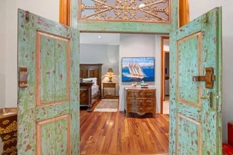 A room with wooden flooring, a bed with a nightstand, a dresser, and a painting of a sailboat on the wall.