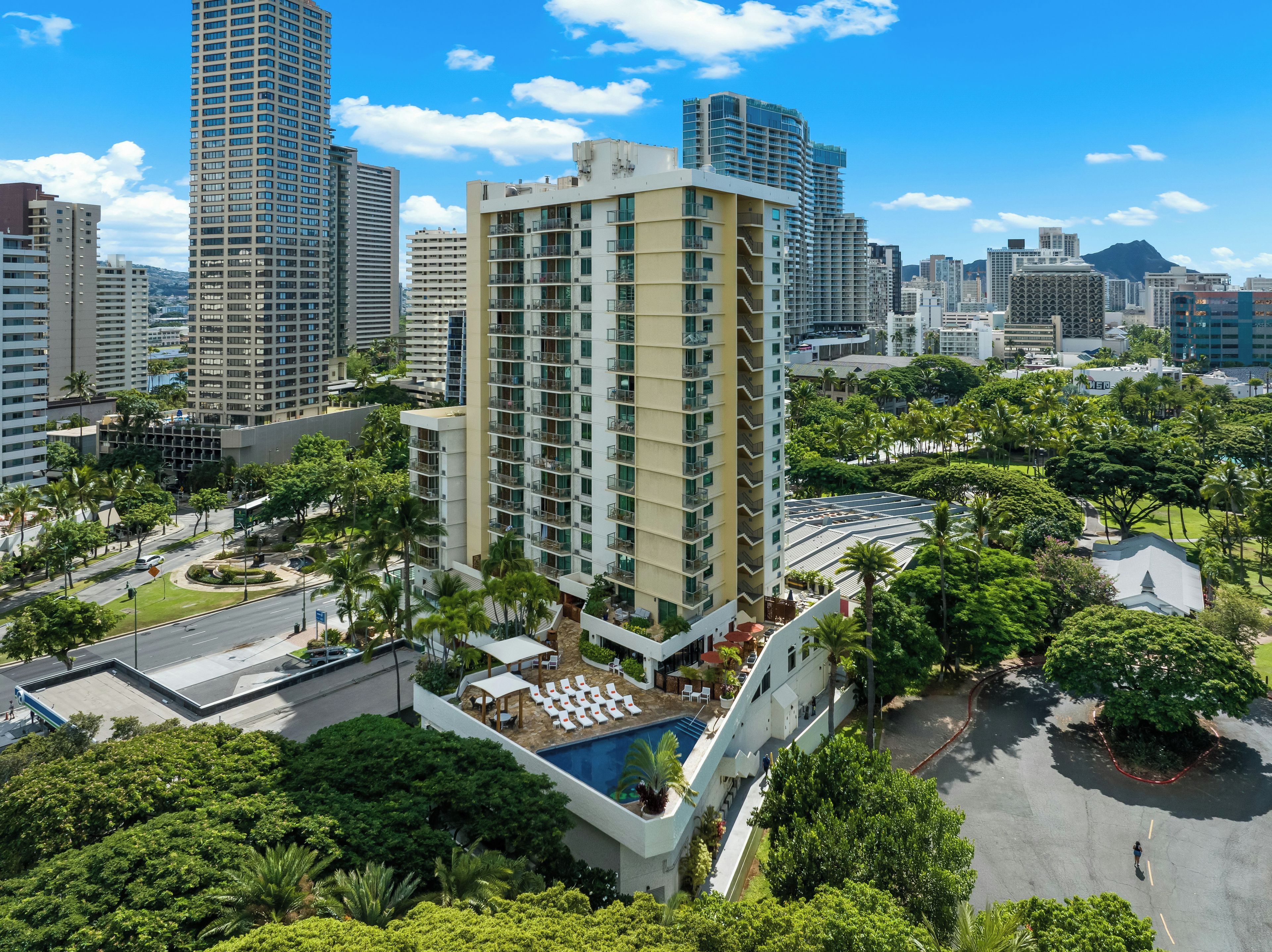 A high-rise hotel with multiple floors, a rooftop pool, and surrounding greenery.