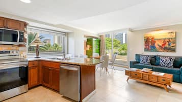 Een moderne keuken met een ingebouwde magnetron, oven en vaatwasser. Er is een zithoek met een tafel en stoelen, en een woonkamer met een bank en een schilderij.