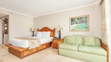 A hotel room with a double bed, a green sofa, a nightstand, a painting of a tropical beach, and a door leading to a bathroom.
