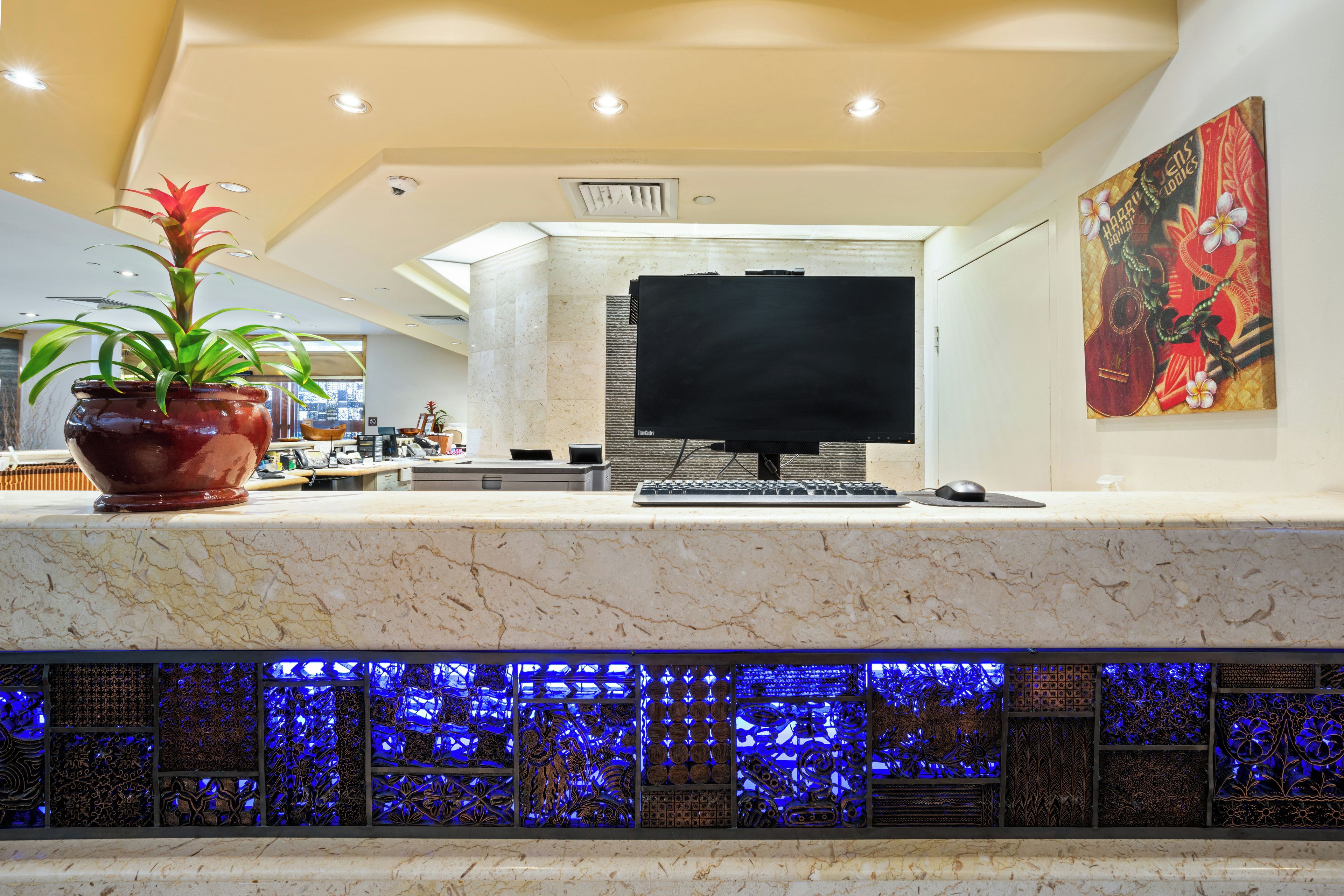 A hotel reception area with a marble counter, a flat-screen TV, a potted plant, and a decorative wall panel.