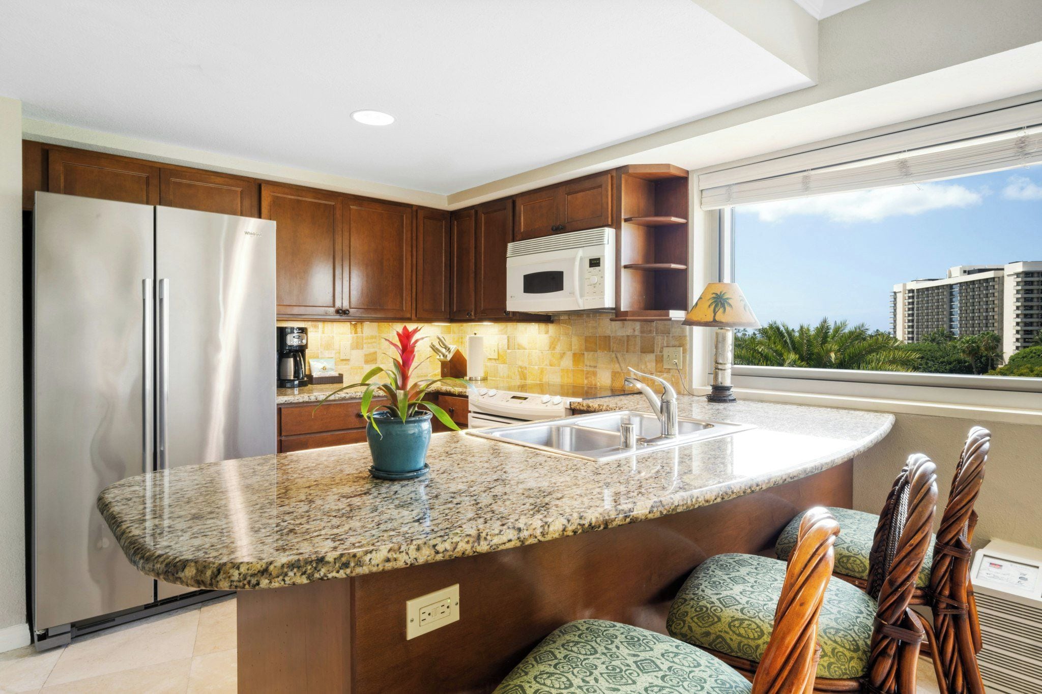 A modern kitchen with granite countertops, a built-in oven, a microwave, and a large window offering a view of high-rise buildings.