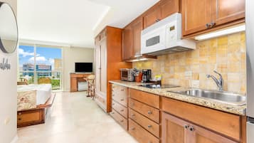 A kitchen with wooden cabinets, a microwave, a sink, and a window overlooking a cityscape.