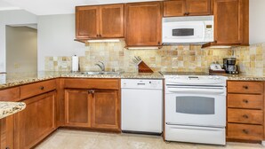 A kitchen with wooden cabinets, a dishwasher, an oven, and a microwave. - Luana Waikiki Hotel & Suites (Honolulu)