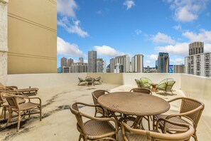 A rooftop terrace with wicker furniture, a round table, and a view of a city skyline. - Luana Waikiki Hotel & Suites (Honolulu)