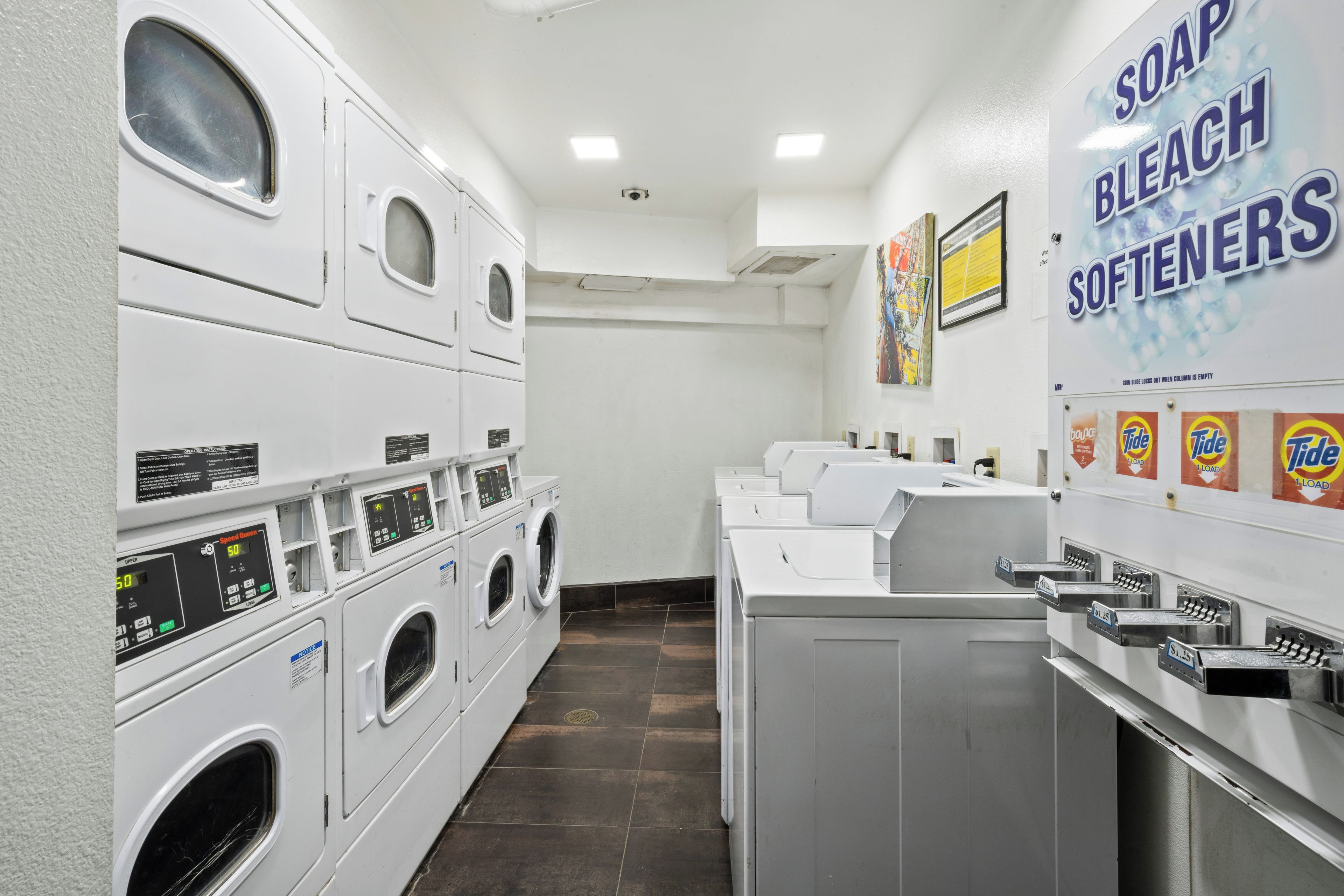 A laundry facility with multiple washing machines and dryers, a soap and bleach softener dispenser, and a Tide detergent dispenser.
