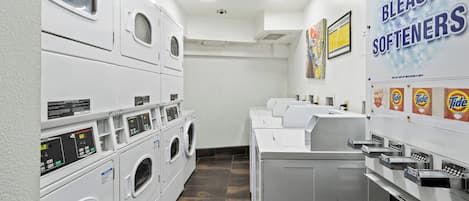 A laundry facility with multiple washing machines and dryers, a soap and bleach softener dispenser, and a Tide detergent dispenser.