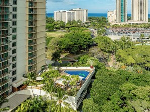 Un hotel de gran altura con piscina en la azotea, rodeado de abundante vegetación y palmeras.