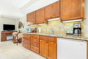 A kitchen with wooden cabinets, a built-in oven, a coffee maker, and a television. - Luana Waikiki Hotel & Suites (Honolulu)