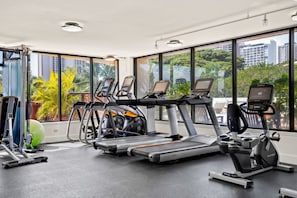 A gym with treadmills, elliptical machines, and a rowing machine, large windows with a city view, and exercise balls.