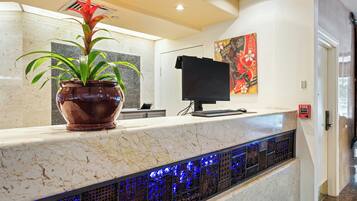 A reception desk with a potted plant, a flat-screen monitor, and a fire alarm sign.
