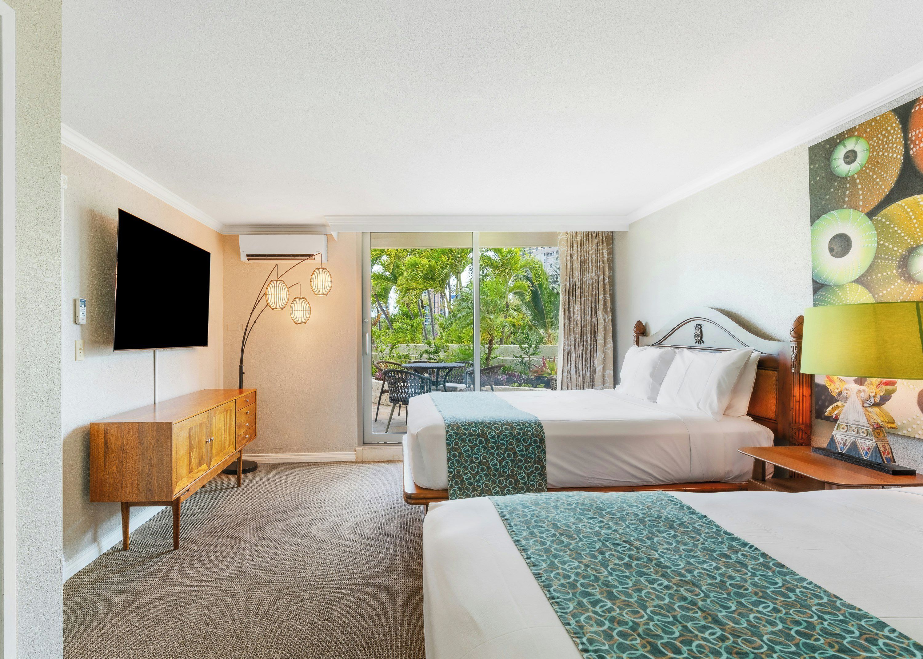 A hotel room with a bed, a desk, a TV, and a view of palm trees.