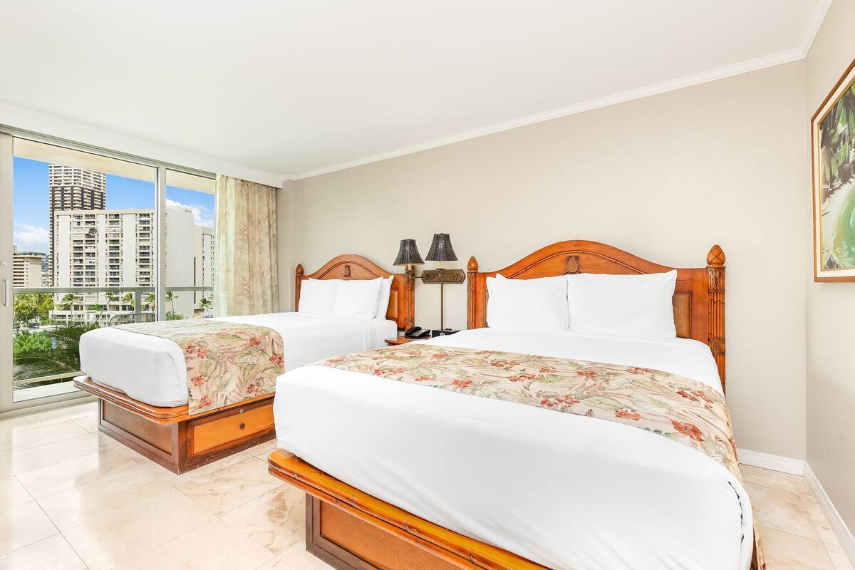 A hotel room with two beds, a large window with a city view, and a painting on the wall.