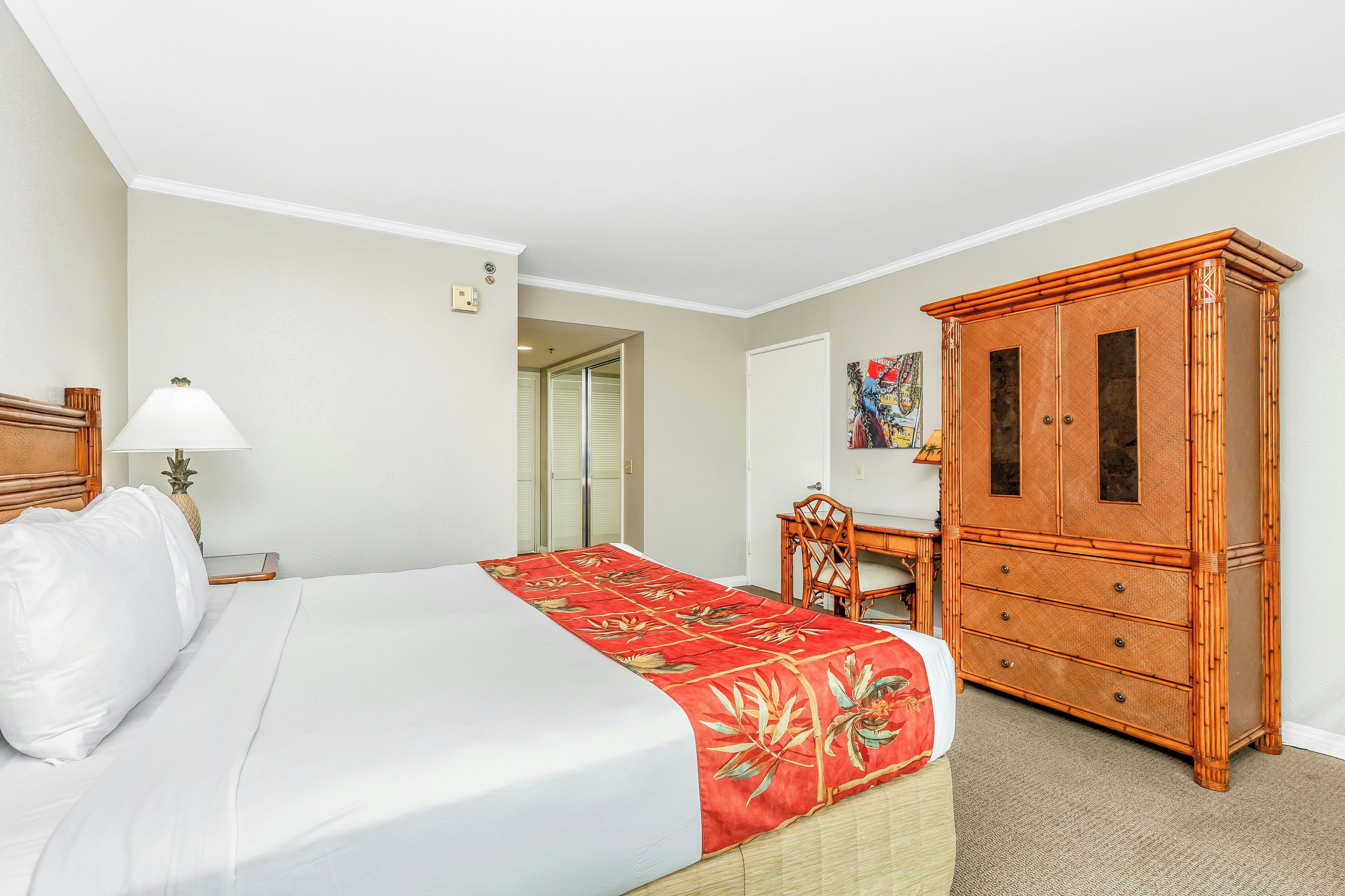 A hotel room with a bed, a desk, a wardrobe, and a door leading to another room.