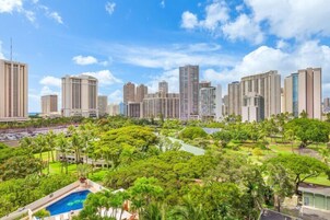 A cityscape with high-rise buildings, a swimming pool, and lush greenery.