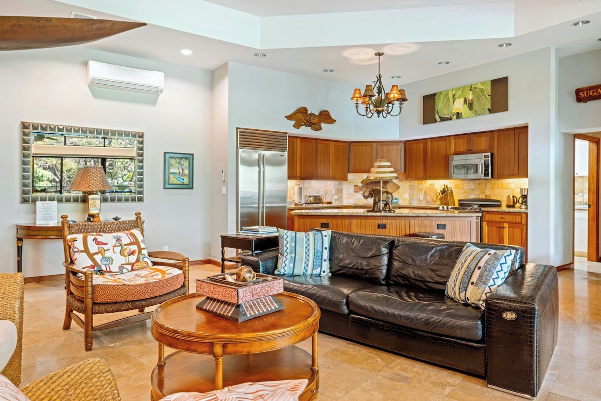 A spacious living area with a leather sofa, a wooden coffee table, and a dining area with wooden cabinets and a kitchen island.