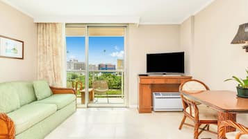 A modern living room with a green sofa, a dining table with chairs, a flat-screen TV, and a view of a cityscape through a glass door.