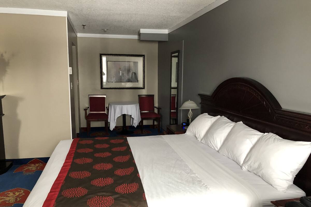 Quarto de hotel com uma cama grande, uma cadeira, uma mesinha e um espelho.