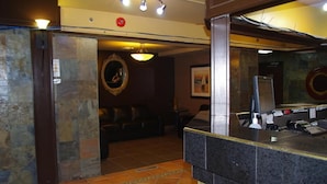 A reception area with a counter, a mirror, a framed picture on the wall, and a seating area with a sofa. - South Hill Lodge (Prince Albert)