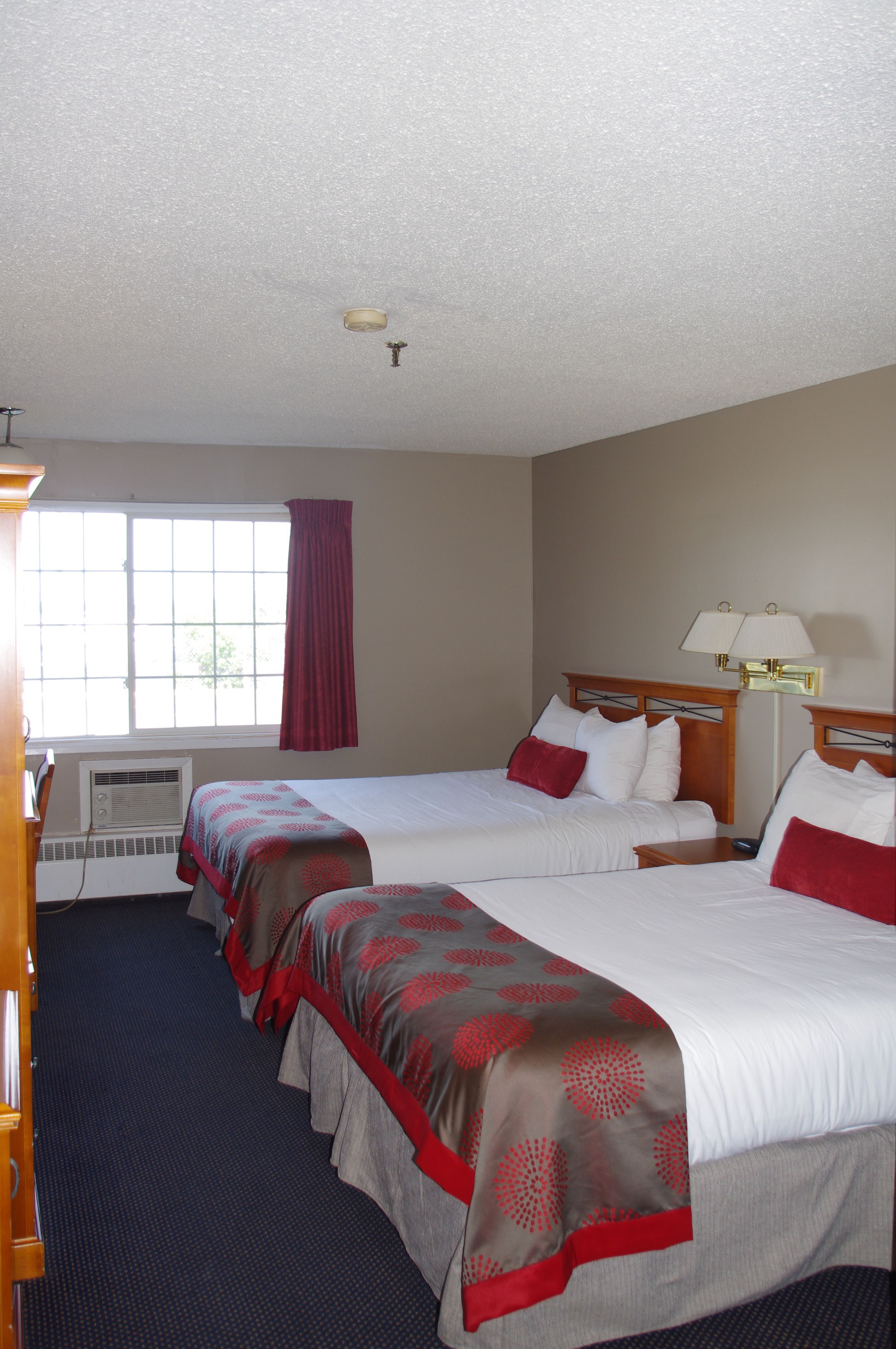 A hotel room with two beds, a window with a view, an air conditioning unit, and a lamp on the nightstand.