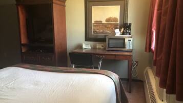 A hotel room with a bed, a desk with a telephone and a microwave, a television, and a radiator.