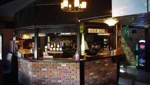A bar area with a brick counter, multiple bottles, and a neon sign. - South Hill Lodge (Prince Albert)