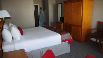 A hotel room with a large bed, a wooden wardrobe, a desk with a lamp, and a chair.