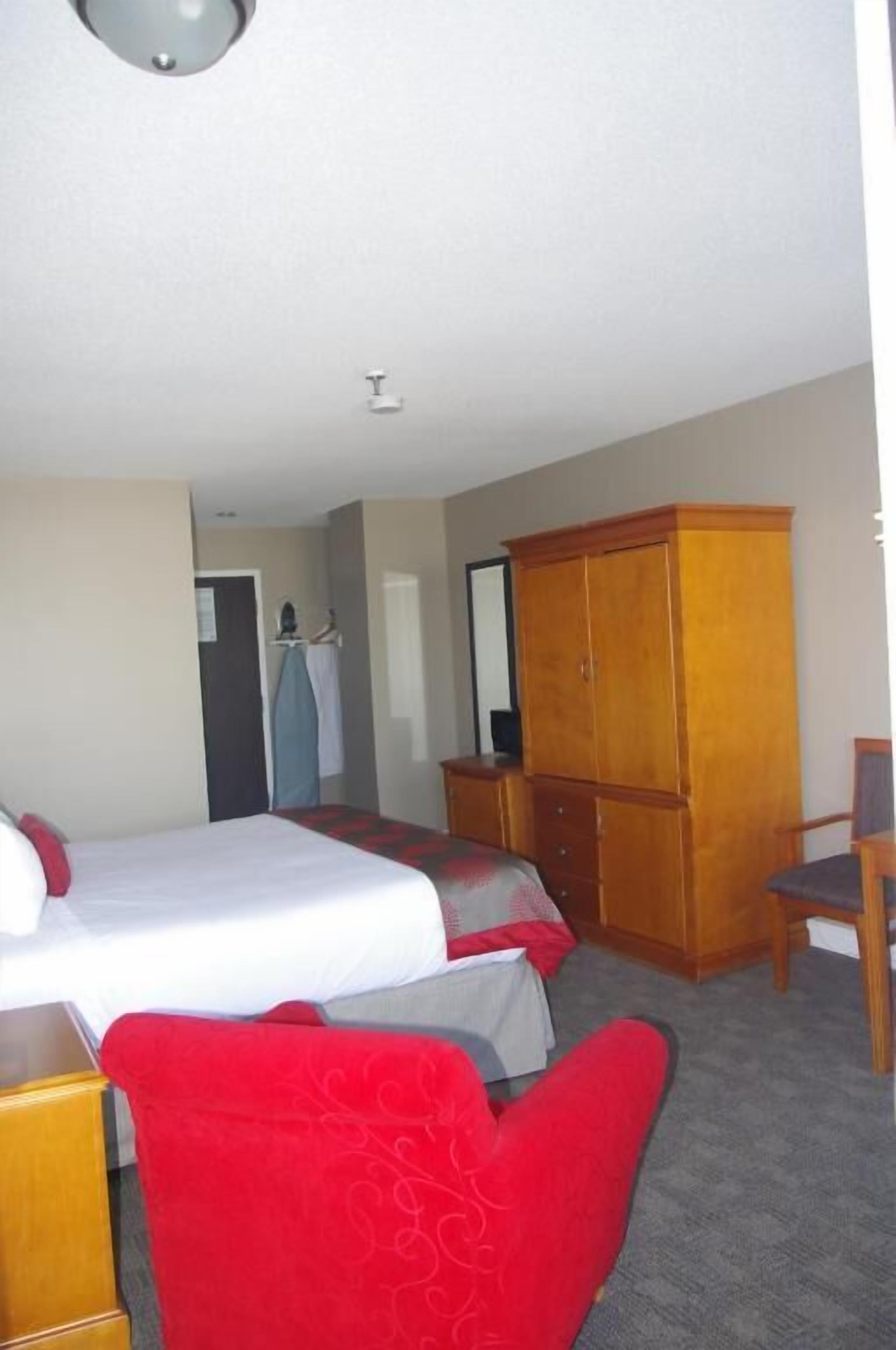 A hotel room with a bed, a wardrobe, a desk, and a chair.