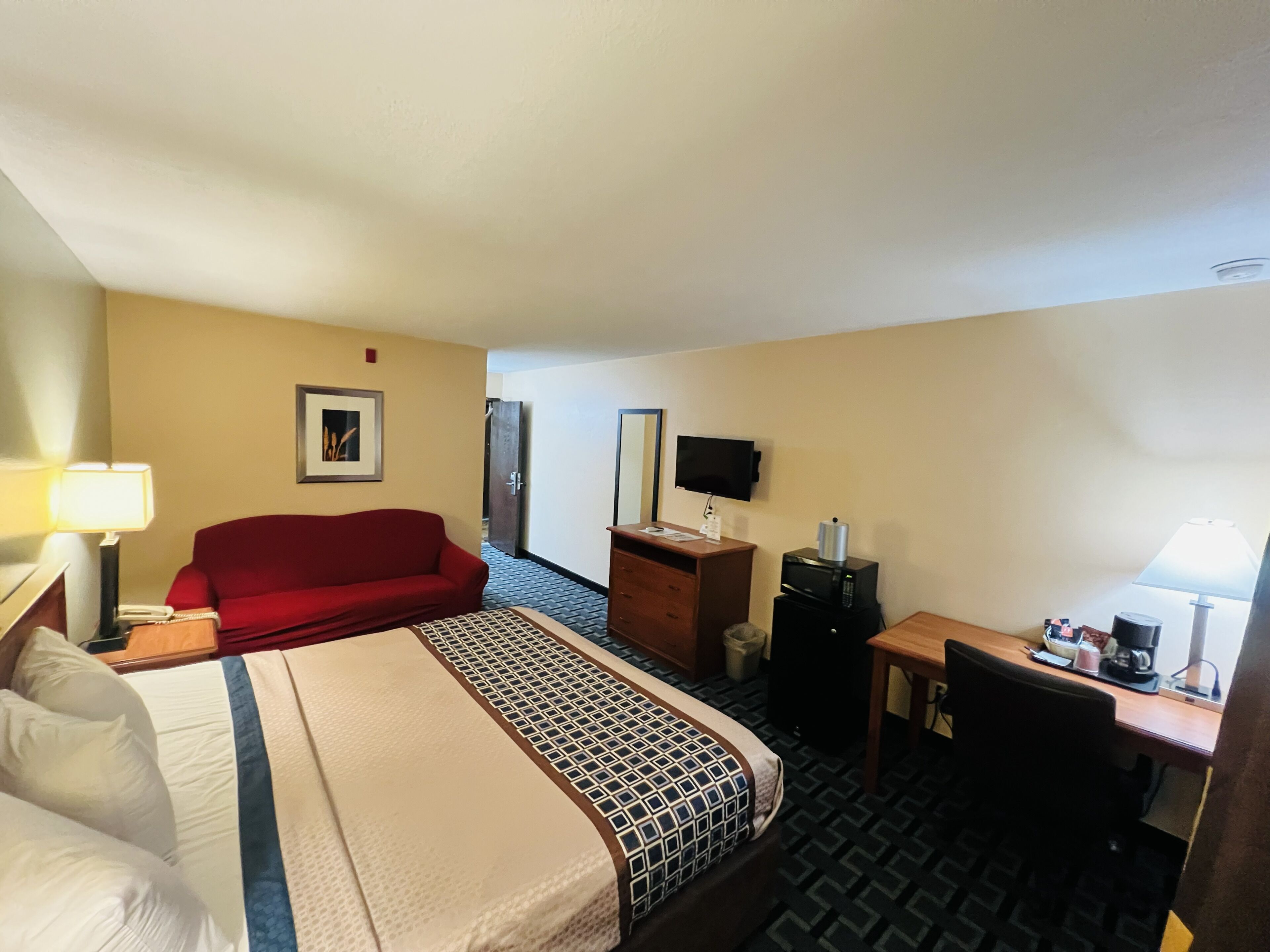 Una habitación de hotel con una cama, un sofá rojo, un escritorio con una computadora, un televisor y una cafetera.