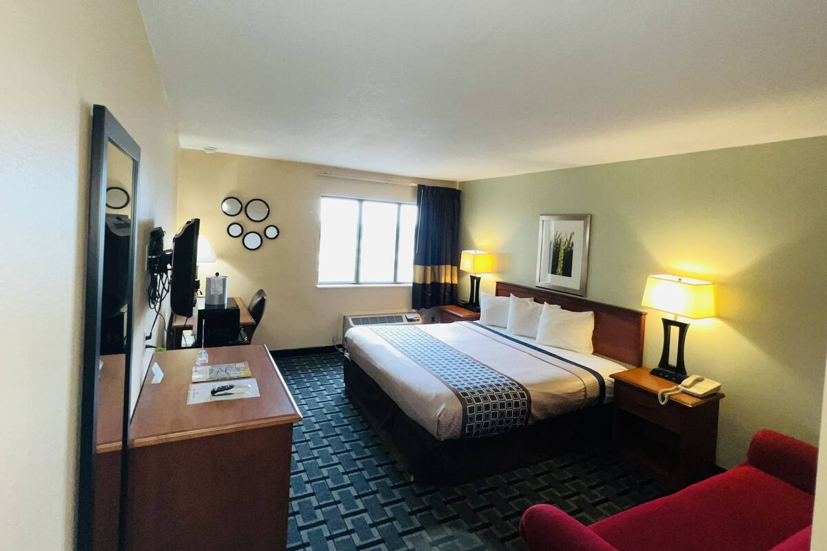 A hotel room with a bed, desk, chair, bedside lamps, and a window.