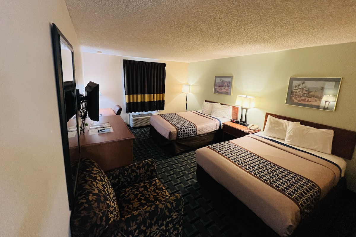 A hotel room with two beds, a desk, a chair, a TV, and a window with curtains.